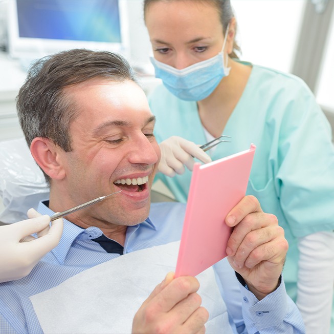 Man looking at smile in mirror after dental restoration