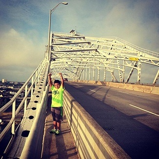 Happy child in green shirt on a bridge with arms in air