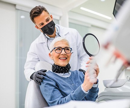 Woman with black glasses smiling at reflection in handheld mirror