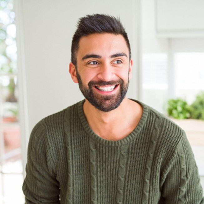 Man in green sweater standing in kitchen and smiling