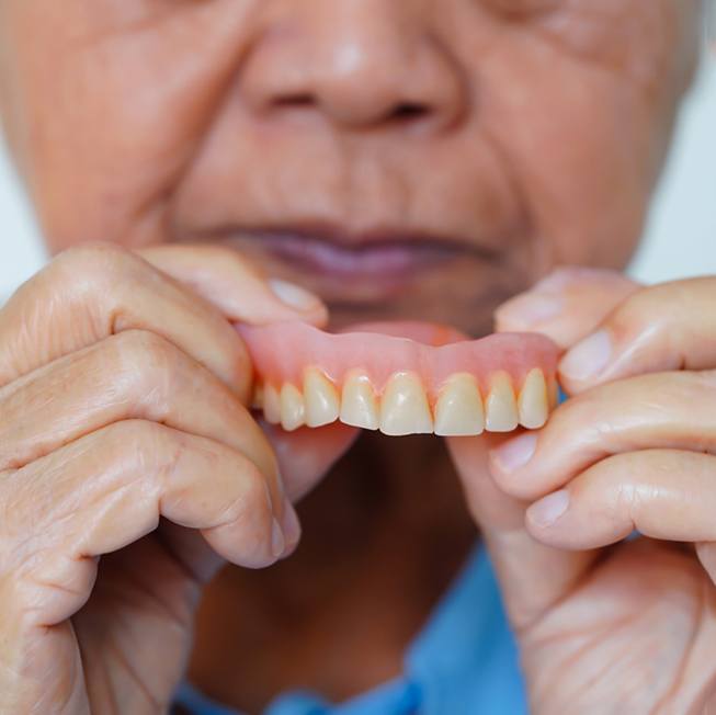 A senior woman holding a denture