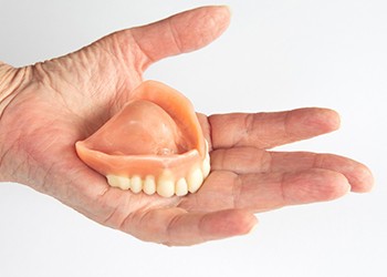 Hand holding denture on white background