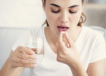 woman taking a pill with a glass of water 