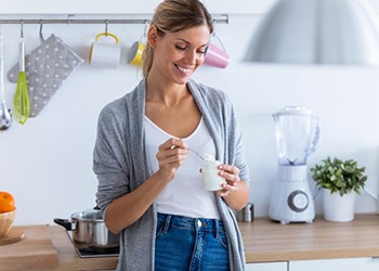 woman eating yogurt standing in her kitchen 