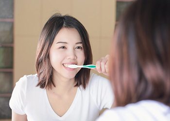 woman brushing her teeth in a mirror 