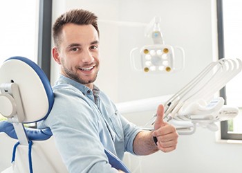 man sitting in dental chair and giving thumbs up 