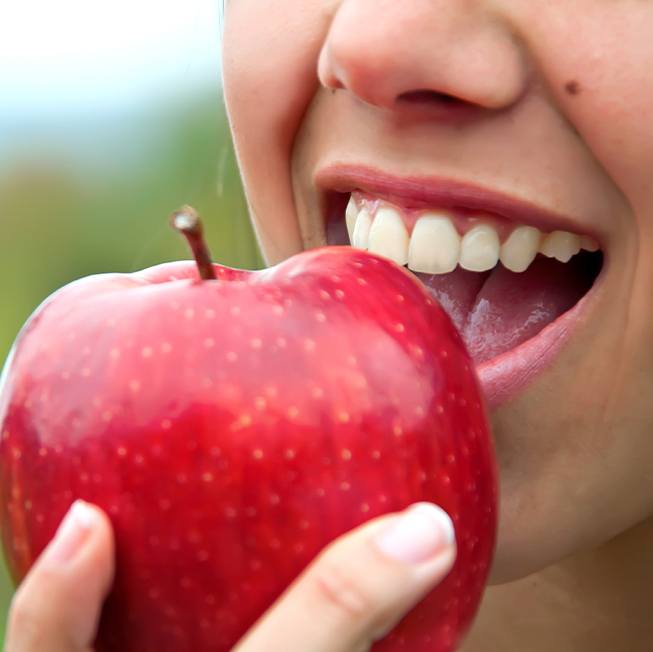 Woman eating a red apple after dental implant tooth replacement