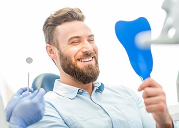 Man smiling into hand mirror after Invisalign in Corpus Christi