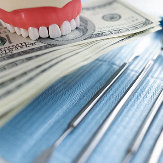 a plastic model of teeth biting down on money sitting next to dental tools
