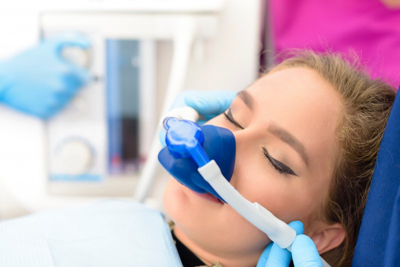 Woman with eyes closed in dental chair with nitrous oxide mask over nose and mouth